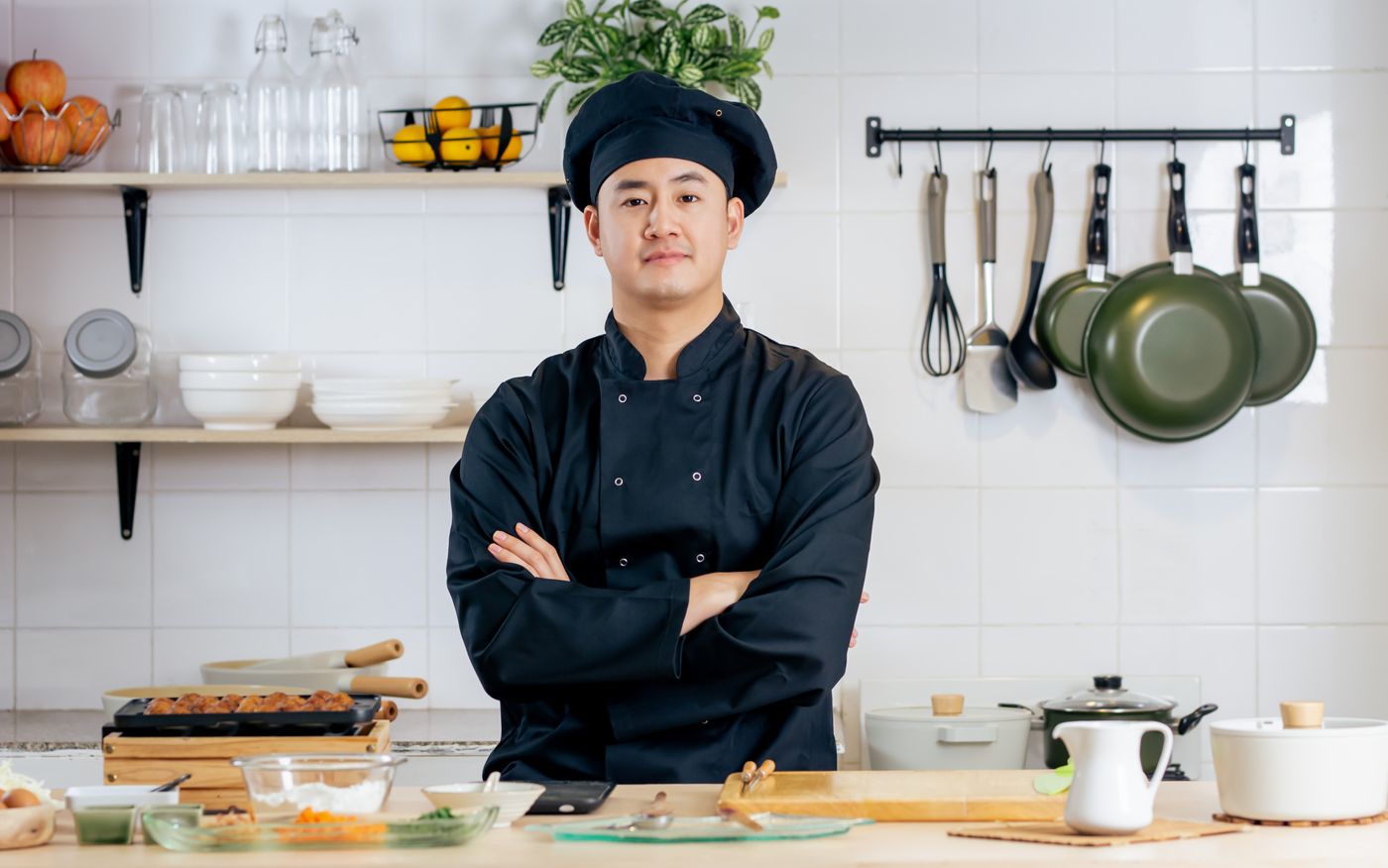 Chef in a black uniform standing with arms crossed in a kitchen